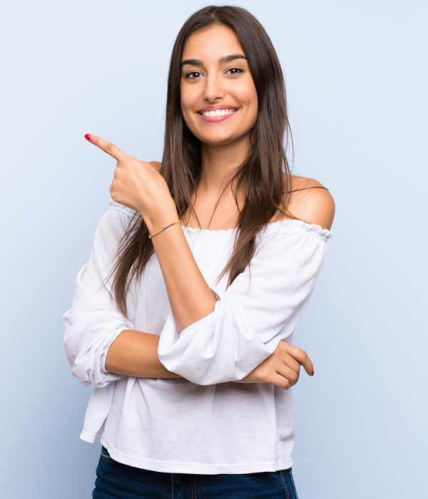 Young woman over isolated blue background pointing finger to the side